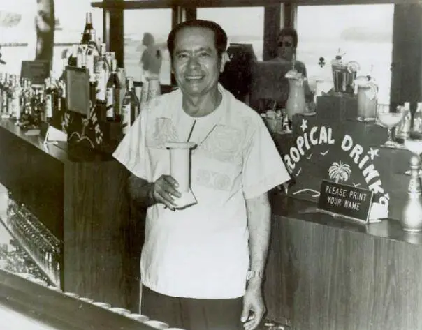 Puerto Rican bartender Ramon "Monchito" Marrero standing front of a bar holding a tropical drink.