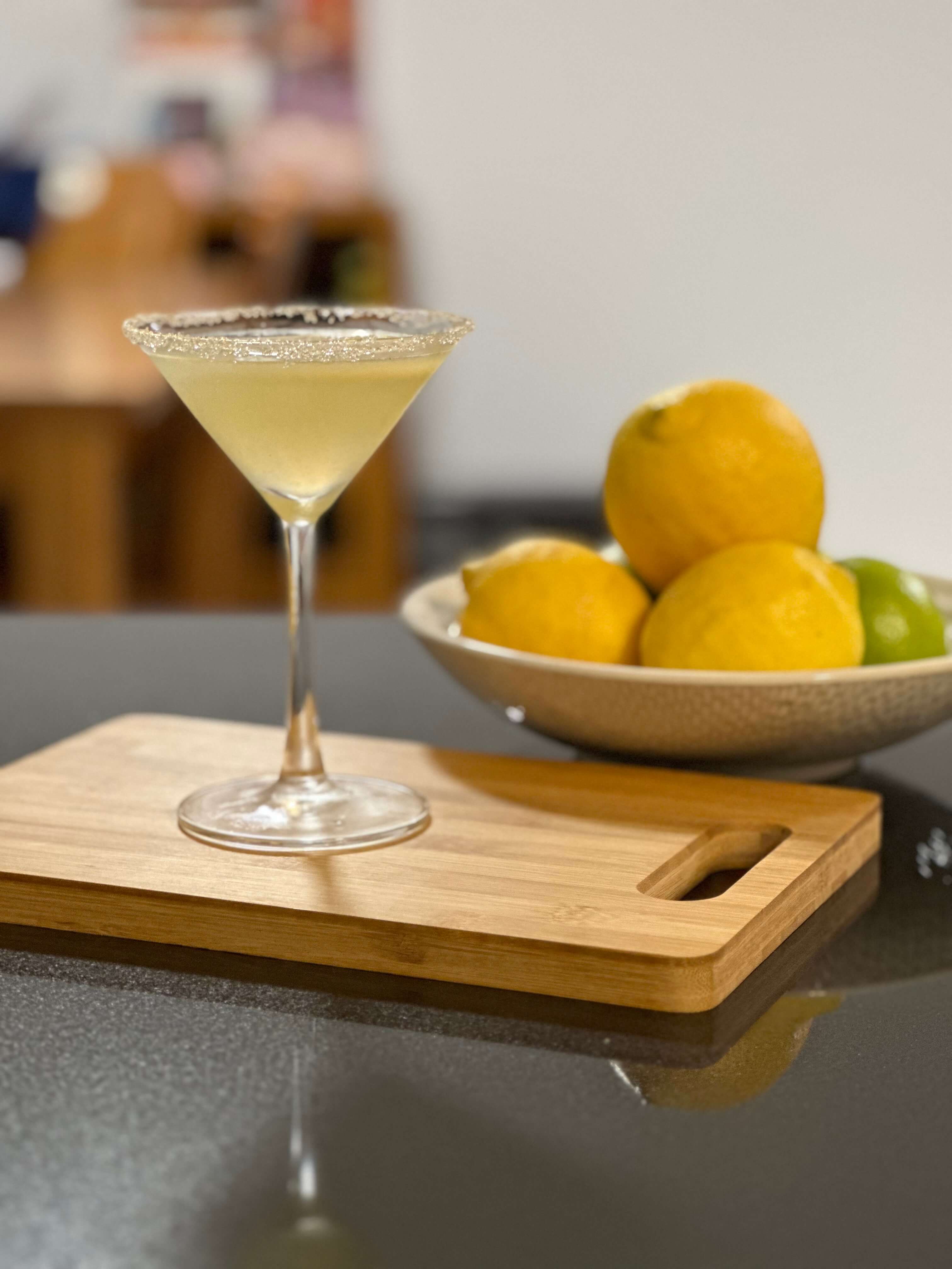 A handmade lemon drop martini posed with bowl of lemons and limes.