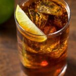 A Cuba Libre, a glass of rum and Coca-cola garnished with a lime wedge.